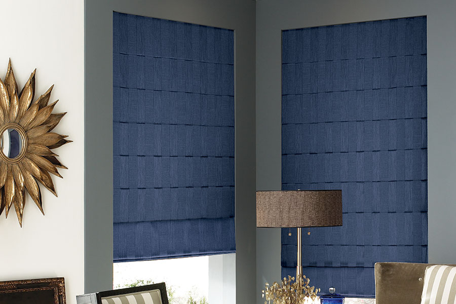 Cordless motorized Roman shades make these beautiful window treatments even easier to use. Dark blue Roman shades on corner windows in a living room.